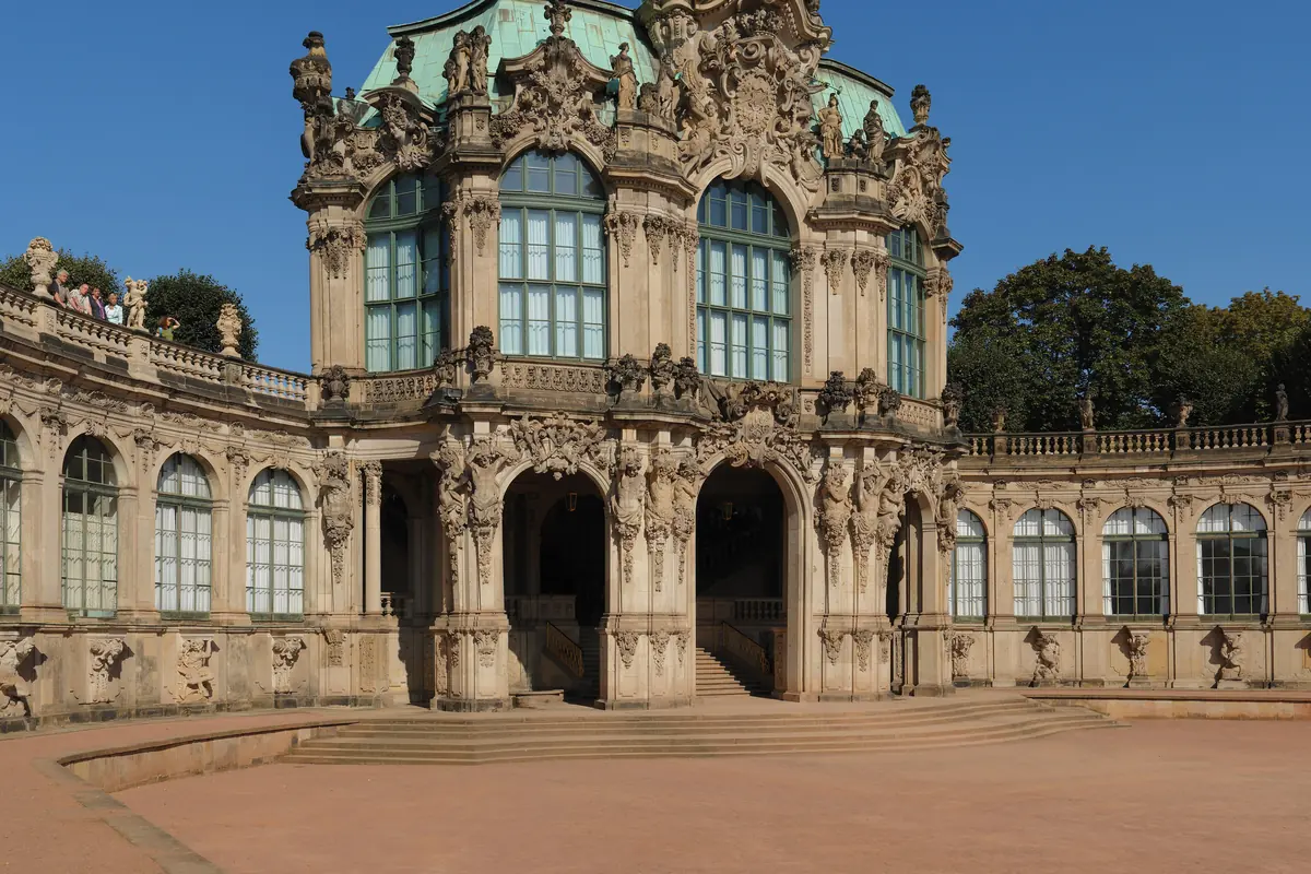 The Wallpavillon seen from the courtyard against a blue sky, with a pair of arched entrances at ground level and a curved gallery beside it.